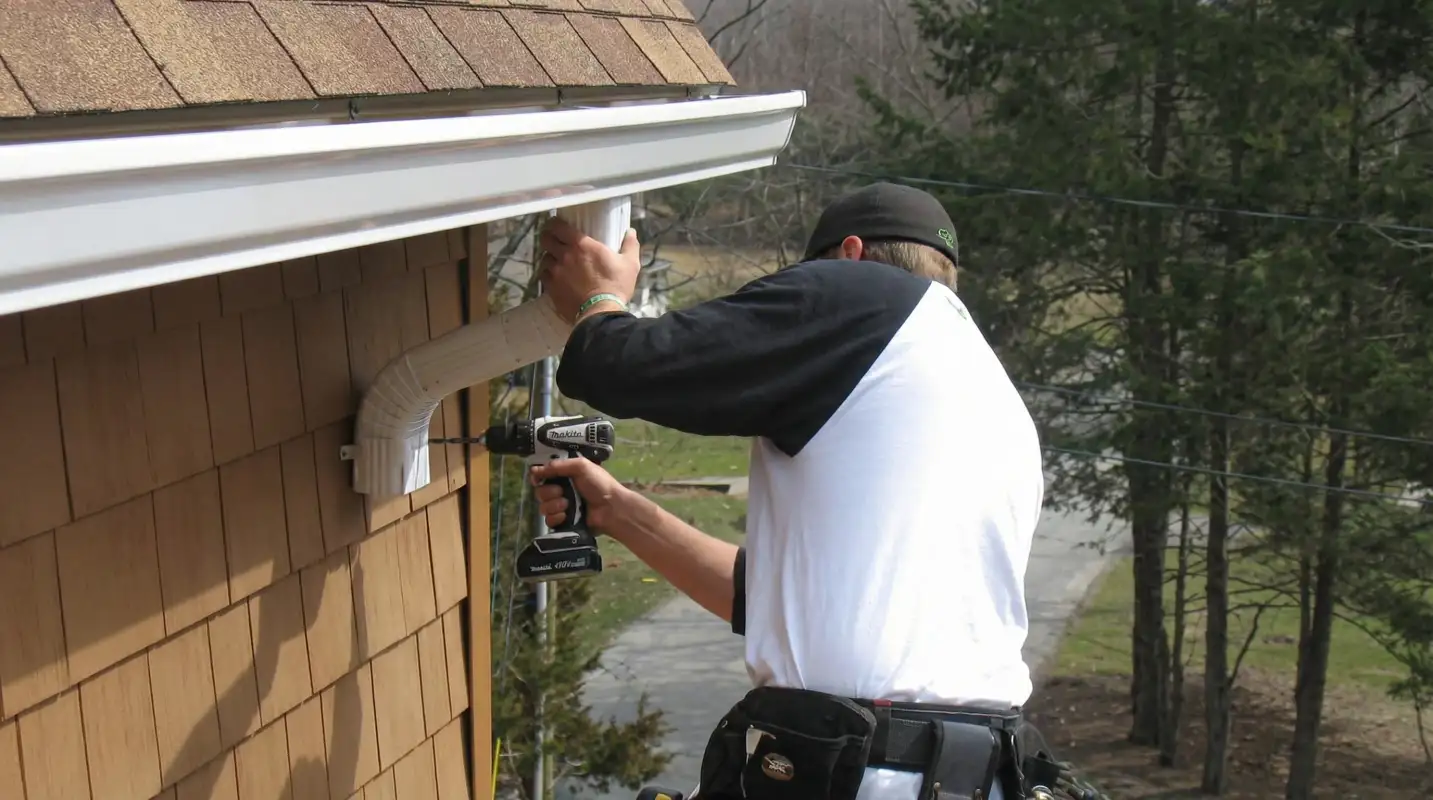 Professional contractor installing tan vinyl siding panels on a residential home exterior in Nashua, NH